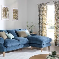 White living room with blue l-shaped sofa and patterned curtains