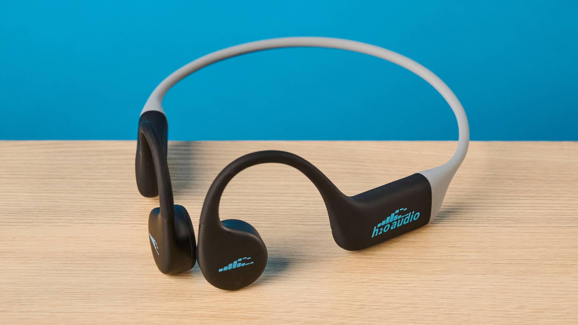 the h2o audio tri run bone conduction headphones photographed against a tom's guide blue background