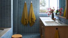 blue tiled bathroom with yellow towels, timber vanity with flowers and built-in bathtub