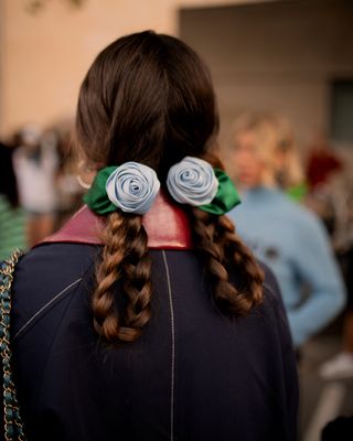 a guest at copenhagen fashion week wears two rosette hair clips pinned into her braids