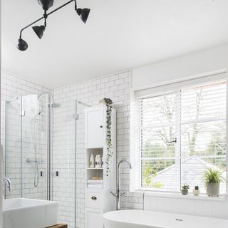 Bathroom with white walls bath, sink, and cabinets, glass shower, grey stone floor, black radiator and light, and wood sink base