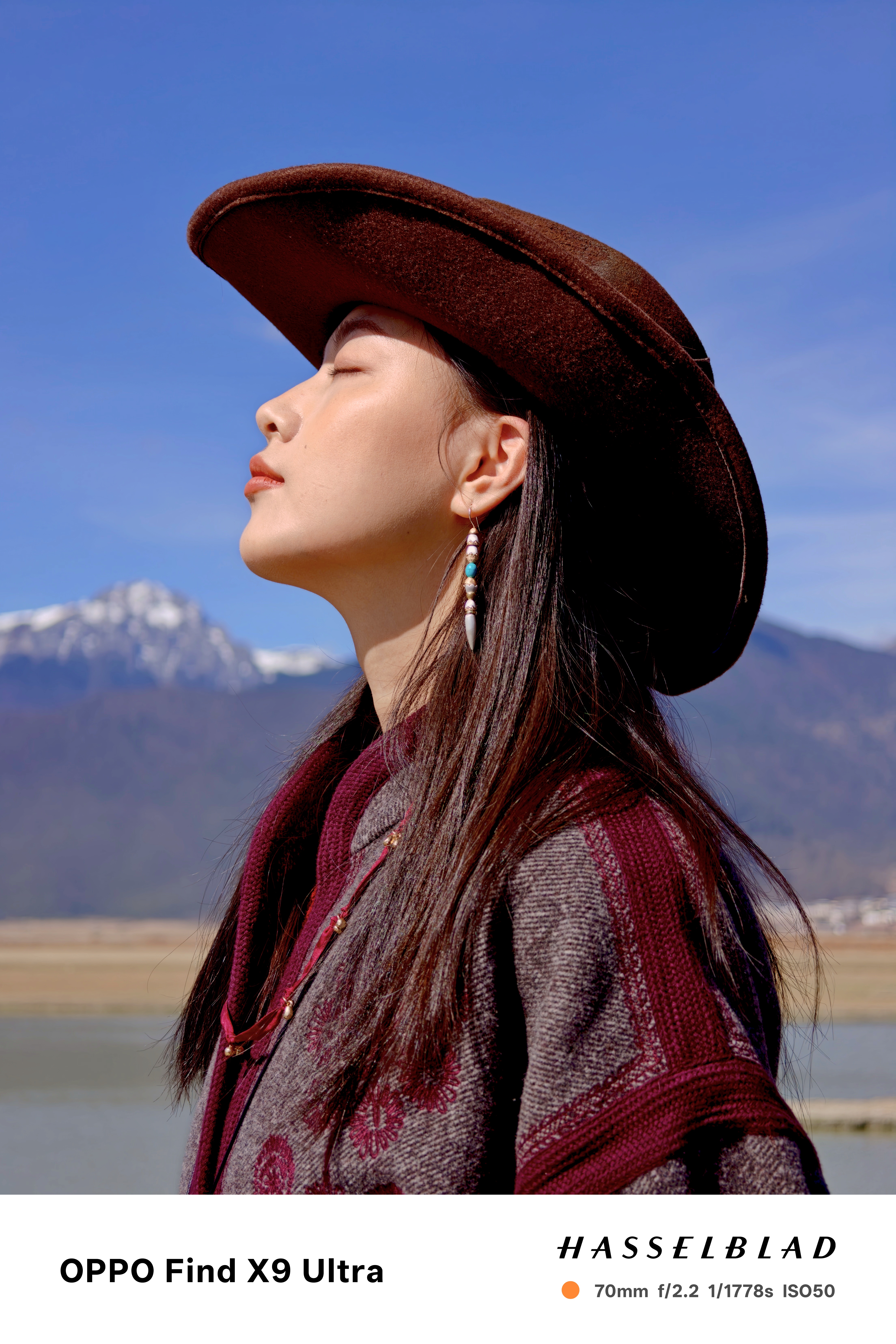 Chinese woman in a cowboy hat posing for a photo with a snoy mountain backdrop