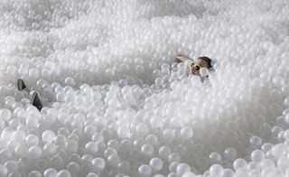 Person lying half submerged in white translucent plastic balls depicting sea