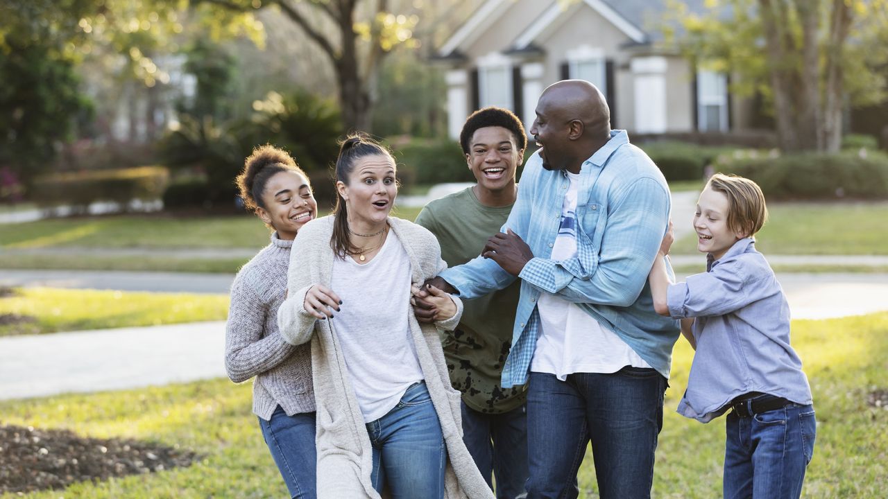 Members of a blended family smile and laugh as they goof around outside their home. 