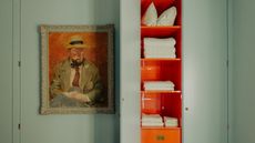 Image of a teal built-in closet with a skinny door that is open to reveal shelving painted in a bright orange color