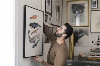 Man hanging a framed print onto his wall at home.