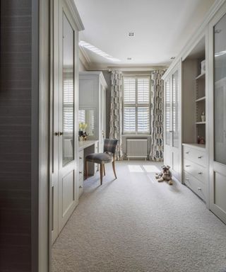 A dressing room with white ceiling and cabinets, sisal carpet, grey walls and chair, and terrier dog lying on the floor.