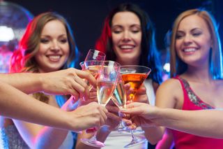 Three women toast with their drinks.