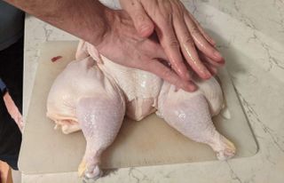 two hands flattening chicken on cutting board