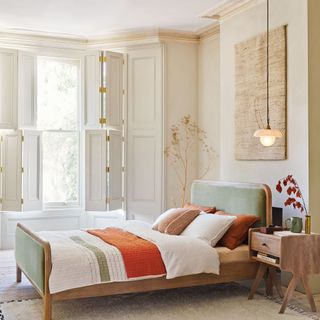 White bedroom with blue bed, layered in white bedding and orange throw