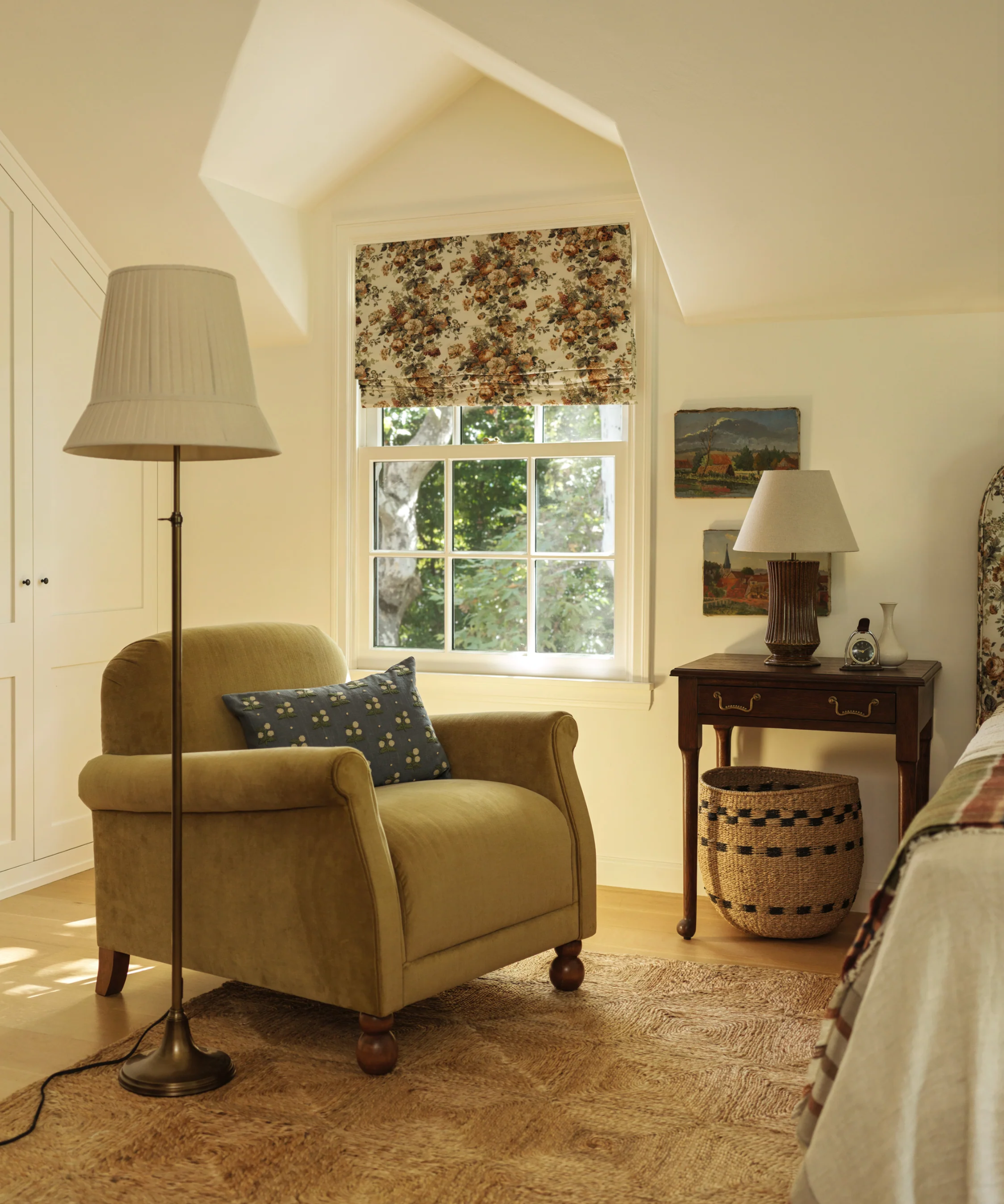 a bedroom with a velvet yellow armchair, a floor lamp, a nightstand, and a woven basket beneath