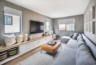 long and narrow gray living room with TV, sectional gray sofa, storage, textured wallpaper