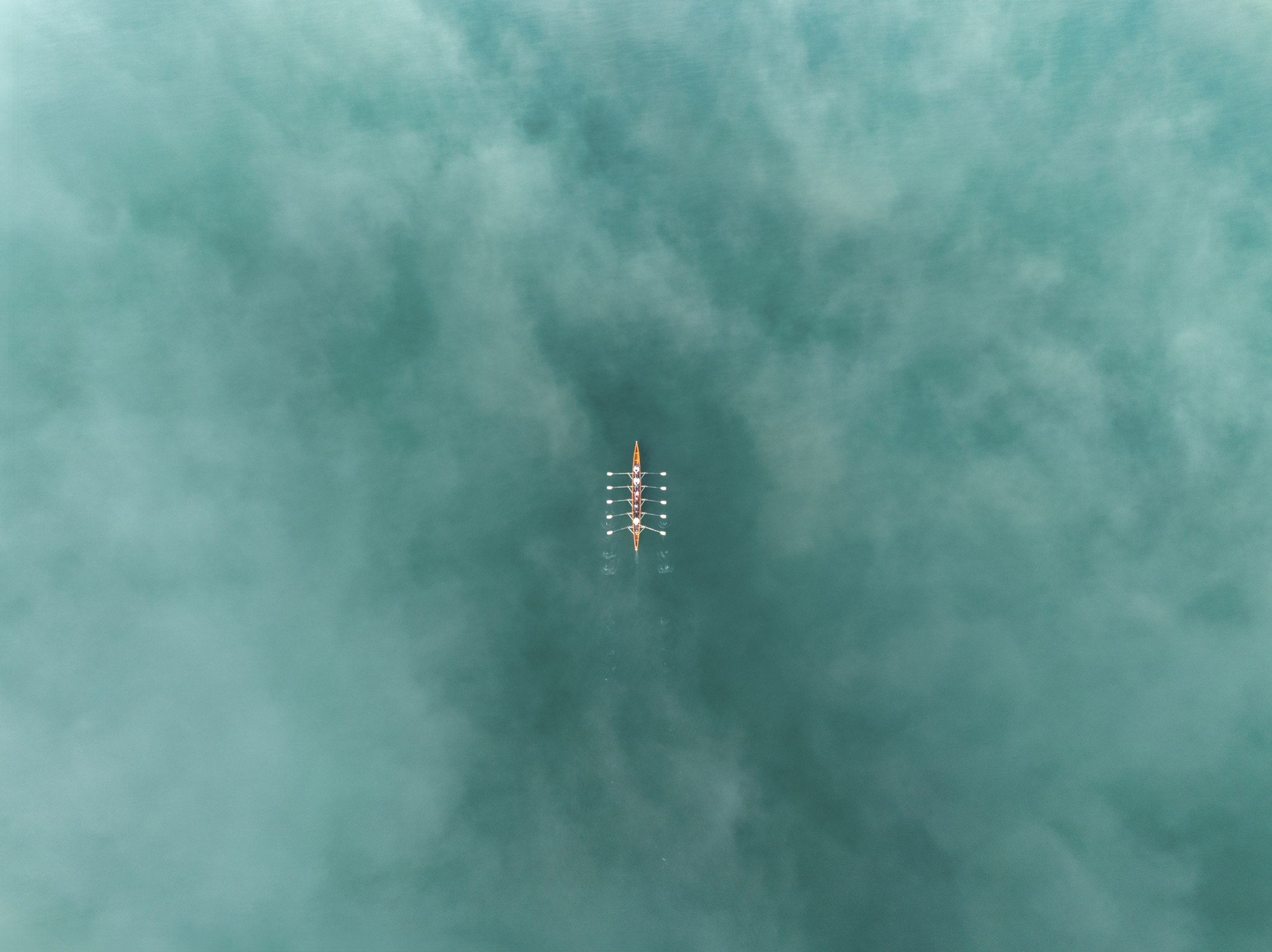 Aerial view of a rowing boat with eight rowers gliding through calm blue-green water
