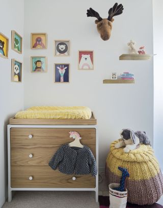 gender neutral nursery with artwork in frames on wall, changing station/chest of drawers, knitted pouffe, floating shelves