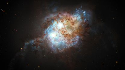Two bright blue spheres representing supermassive black holes swirl amidst a cloud of blue and brown dust in the early universe
