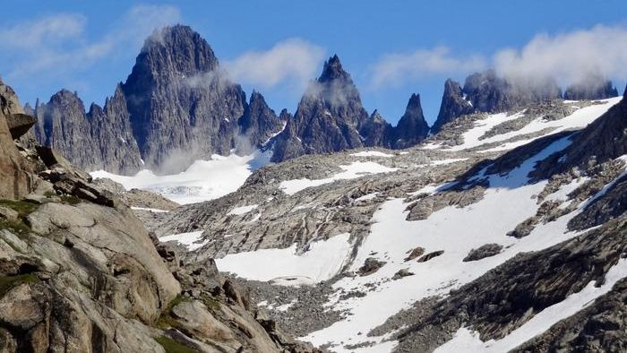 stony moutainous rocks shoot from the ground into a blue sky. snow is settled on the slopes.