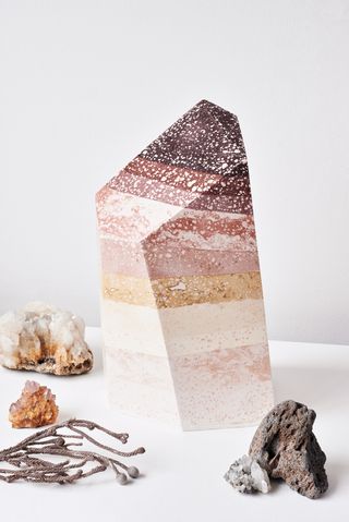 View of Zuza Mengham’s work featuring a tall multicoloured stone, smaller crystals and a twig style piece pictured against a light grey background