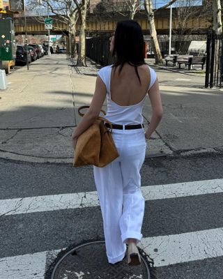 Mimi Nguyen wearing an all-white outfit and carrying a camel suede handbag
