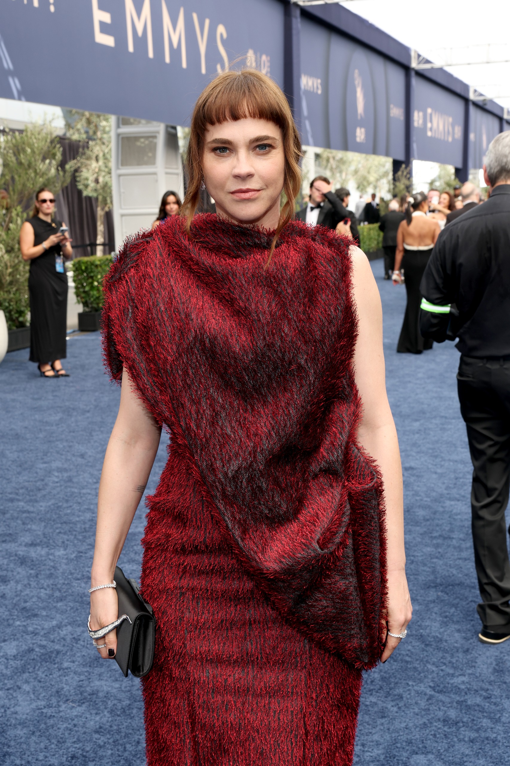 a woman with red hair in a red dress on the blue emmys carpet