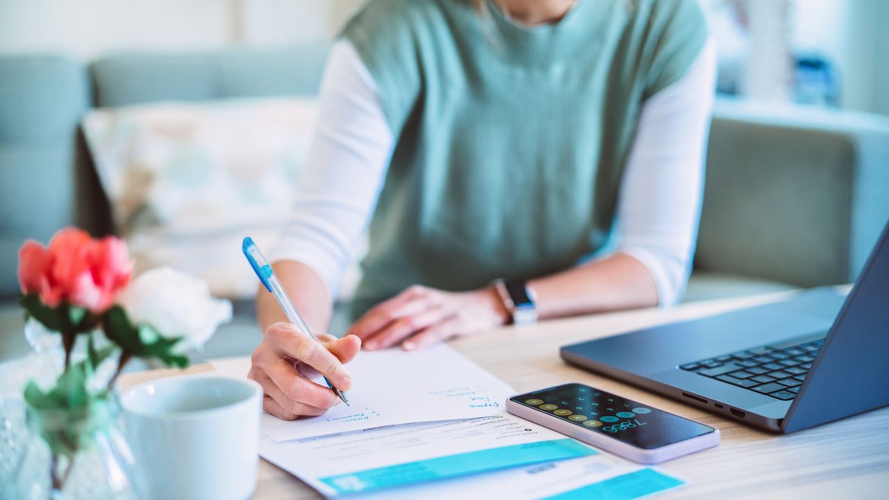 A woman works on tax planning with her laptop, paperwork and calculator.