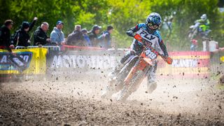 A motocross rider in action, riding through a track, and the fast movement is making the dirt fly towards the lens