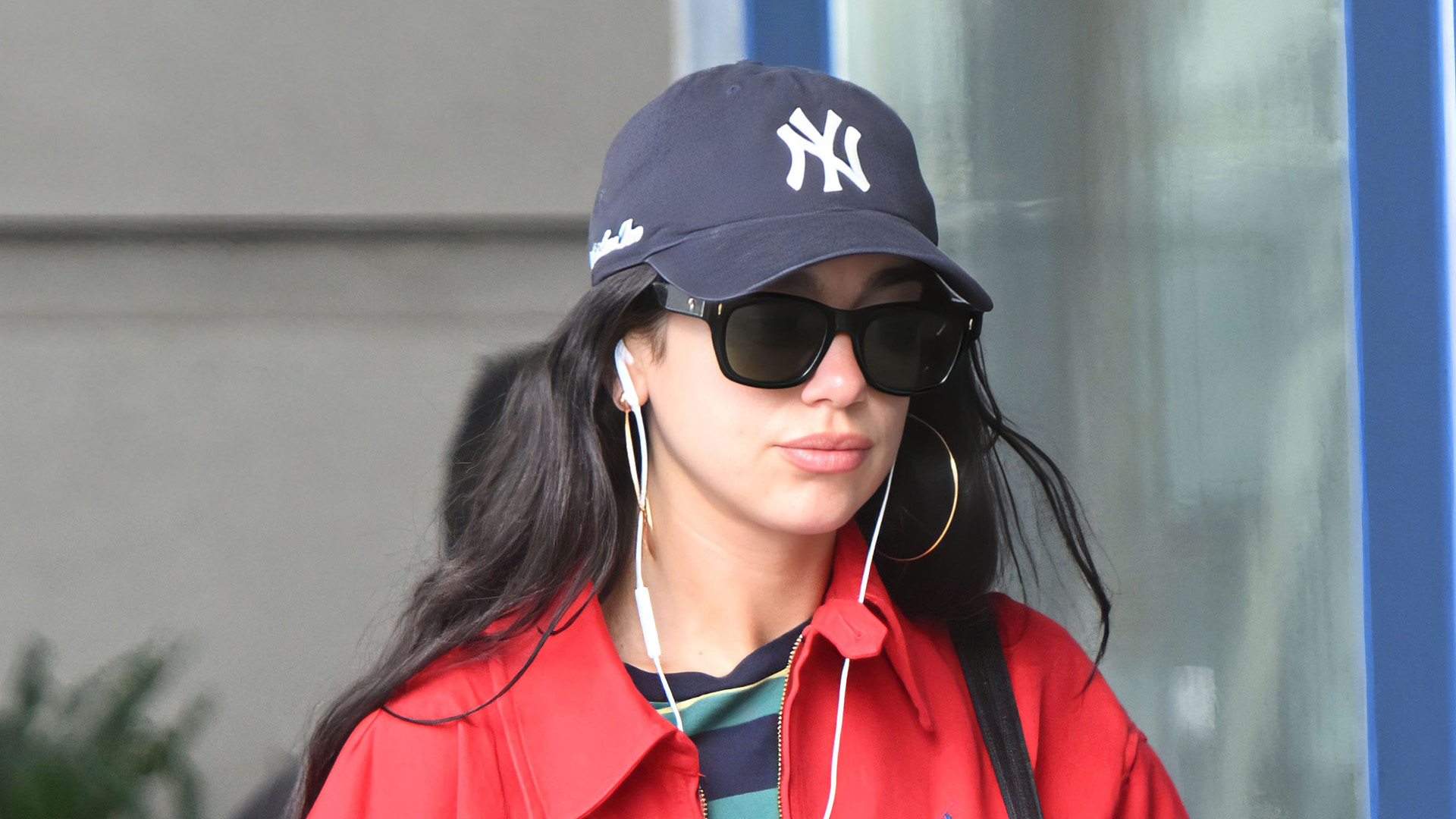 Dua Lipa at JFK wearing a red Polo Ralph Lauren cotton jacket with a retro striped tee, washed-black jeans, black leather boots, and a NY Yankees baseball cap
