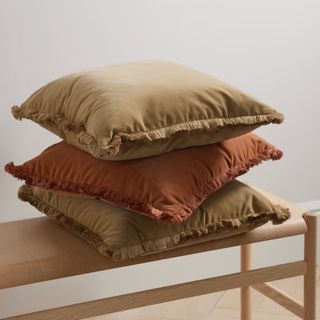 three stacked cushions in neutral colours with fringe