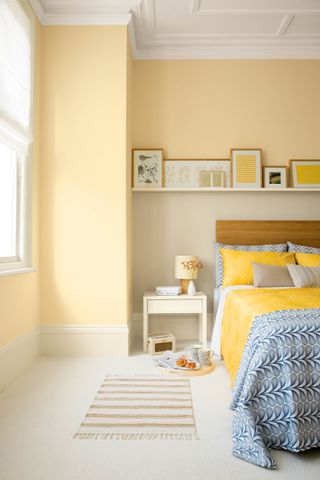 A yellow bedroom with blue bedding and white carpets