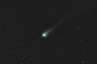 comet glowing green and white with a long tail against a backdrop of stars.