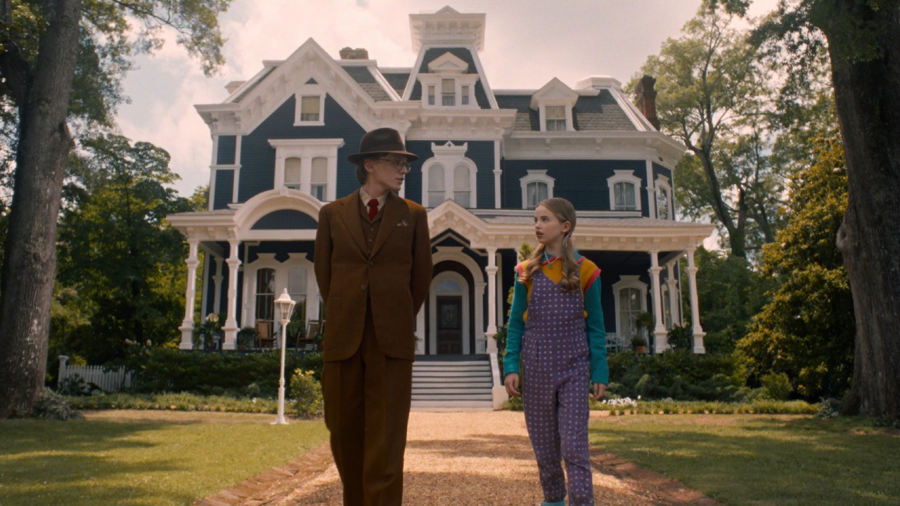 From left to right: Mr. Whatsit walking with his hands behind his back and Holly walking alongside him.