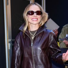 Kristen Bell wearing a brown leather jacket, sash pants, and satin pumps in NYC