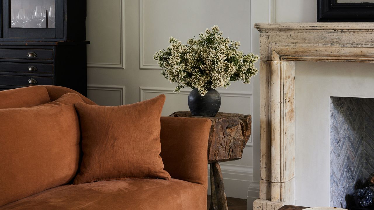 a beige living room with a corner of an amber colored sofa and a rustic fireplace