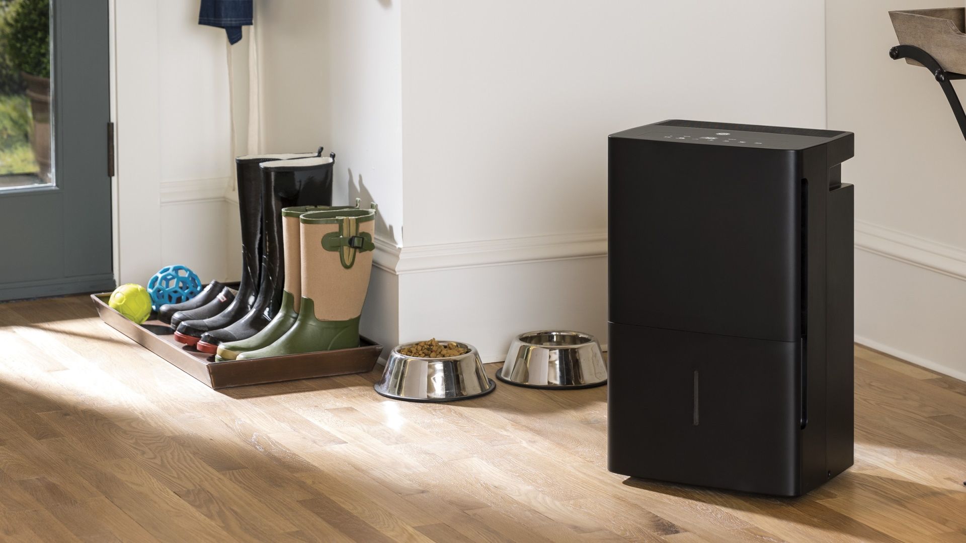 A dehumidifier in a hallway with boots and pet bowls