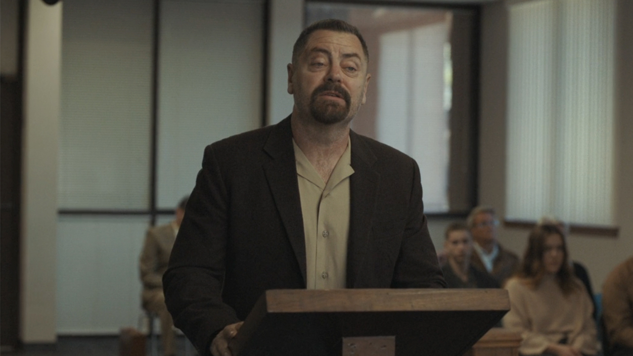 Nick Offerman in a suit, standing at a podium in Sovereign