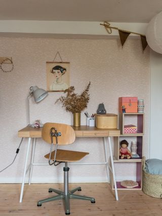 mid-century inspired office with pale pink wallpaper, a wooden desk and chair, and children's accessories and bunting