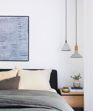 White bedroom with two low hanging concrete pendants, bed with artwork mounted above