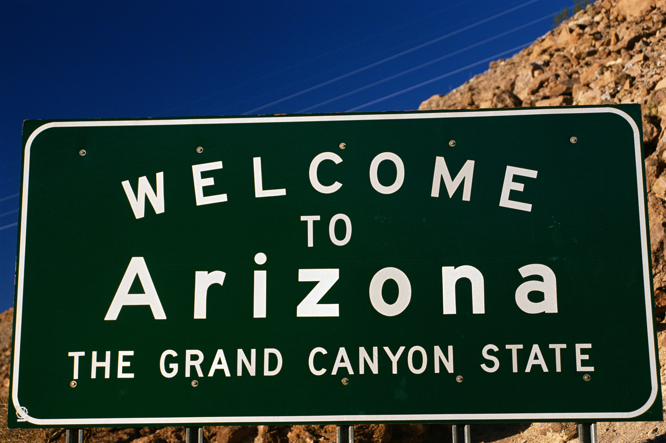 "Welcome to Arizona" state sign with mountains and blue sky in the background