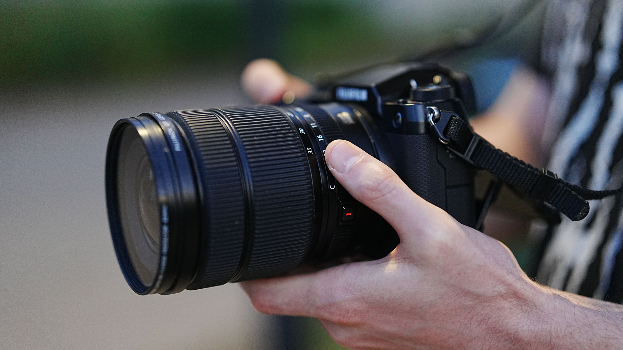 A close-up of hands holding the Fujifilm GFX100S II with the Fujifilm GF 20-35mm f/4 R WR lens attached.