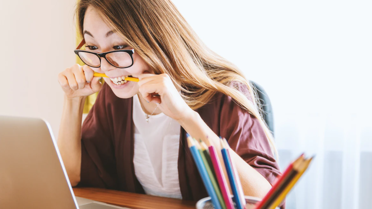 Woman at a laptop biting a pen in frustration or, perhaps, fear of what is to come - the suspense terrible