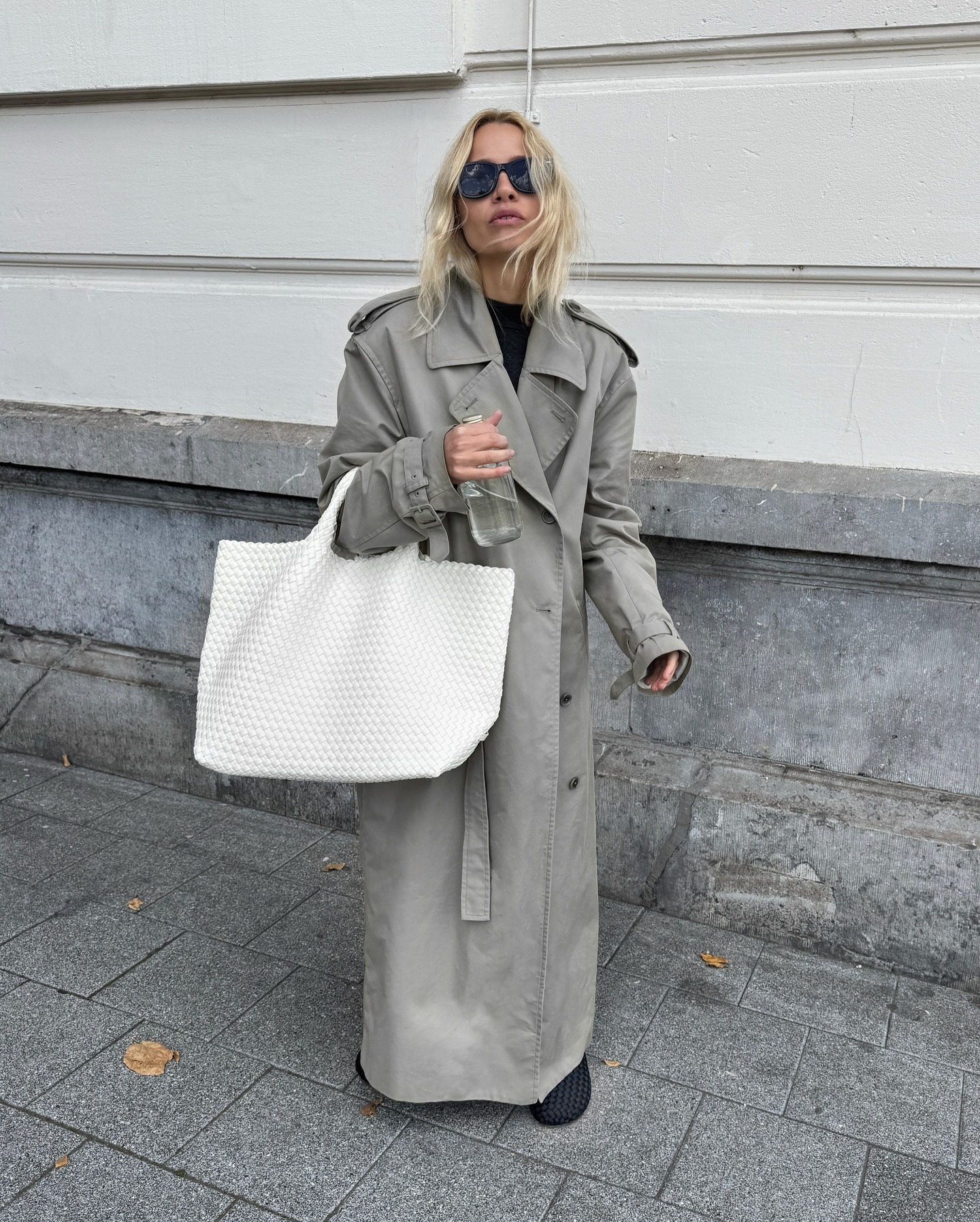 Stephanie Broek wearing a white woven tote against a gray trench coat.