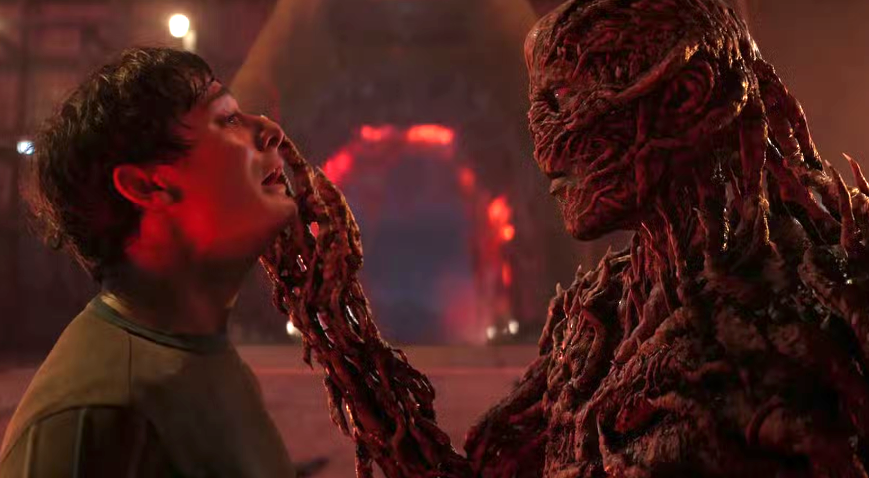 a red-skinned demon paws the face of a teenage boy