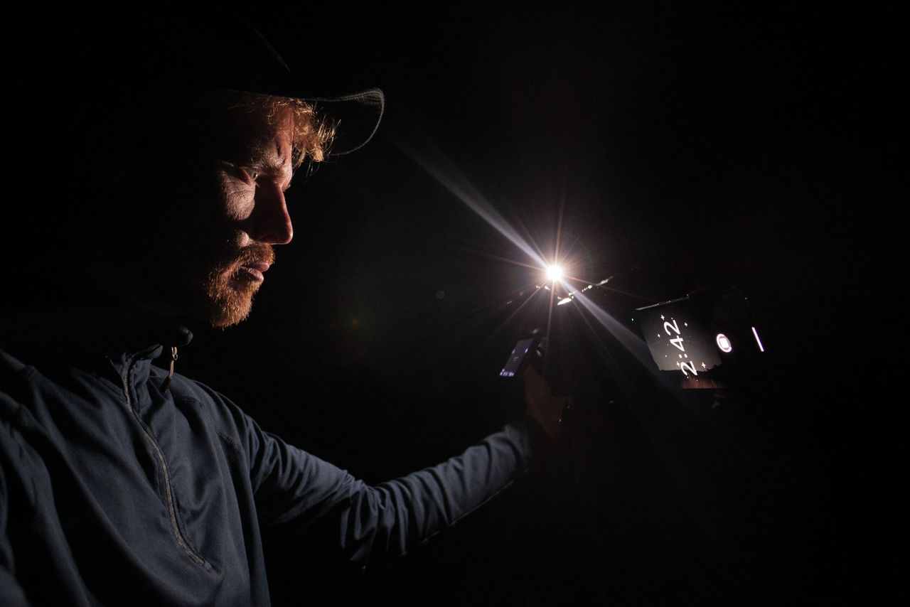 Pixel phone and Nikon mirrorless camera side by side mounted to tripods at night, with the astrophotography mode active on the Pixel and Tim Coleman controlling the camera