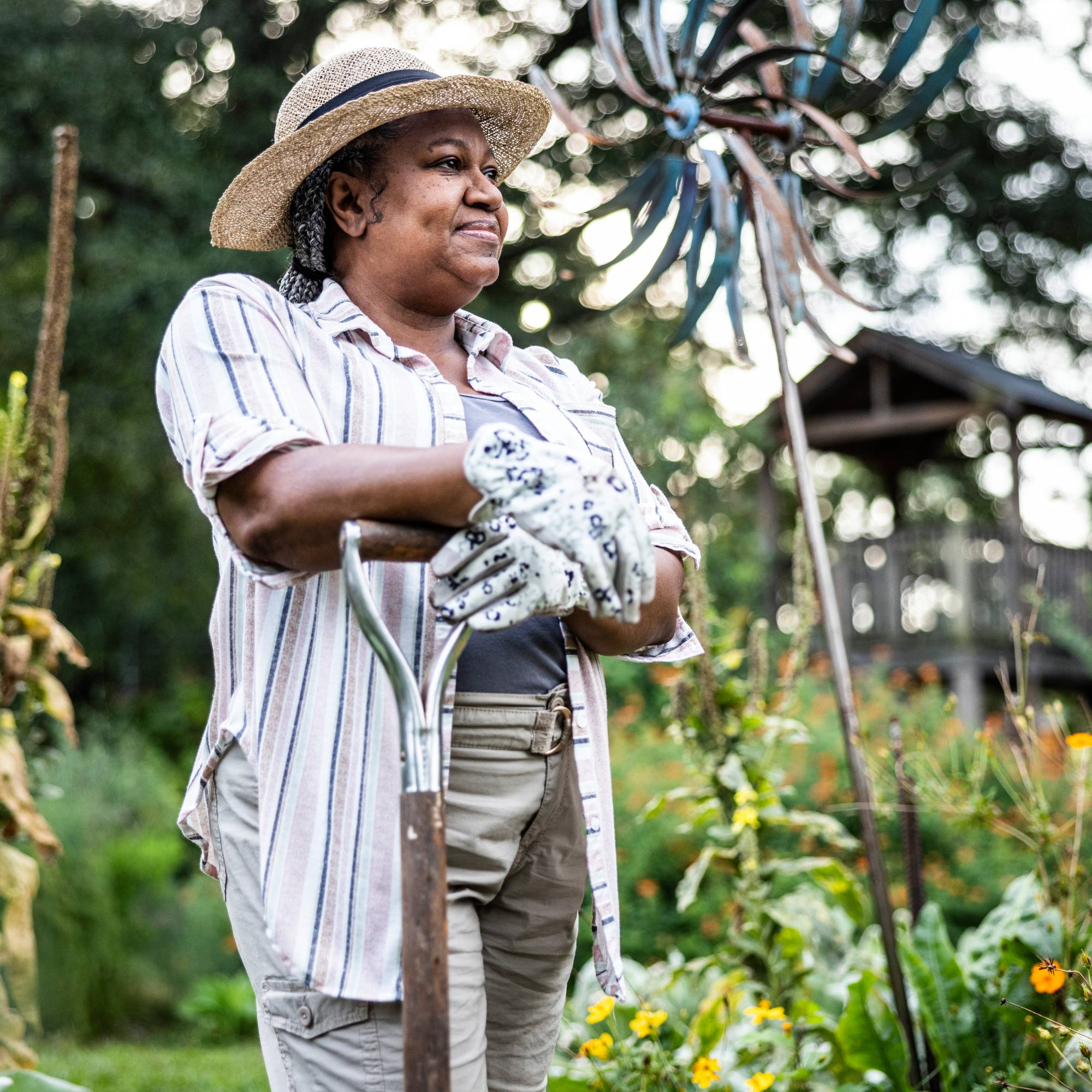 A smiling woman leans on a shovel in a garden