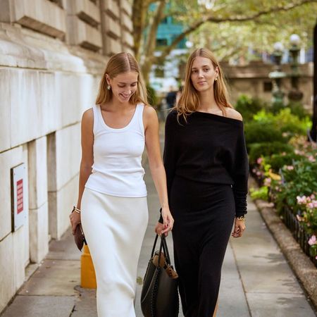 Two friends walk on a sidewalk. One wearing all white and one wearing all black.