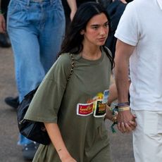Dua lipa wears an oversize graphic t-shirt, denim shorts, a black chanel bag, and black moto boots.