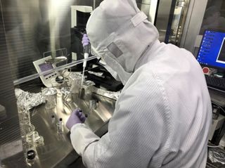 a scientist in a clean suit examines an asteroid sample