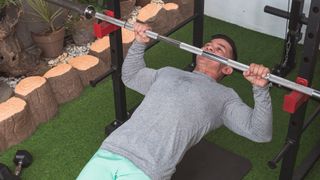 Man performs inverted row using a barbell in a squat rack