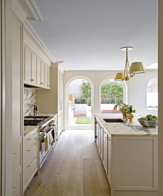 off white kitchen with island, marble worksurfaces, arched doors and wooden floor