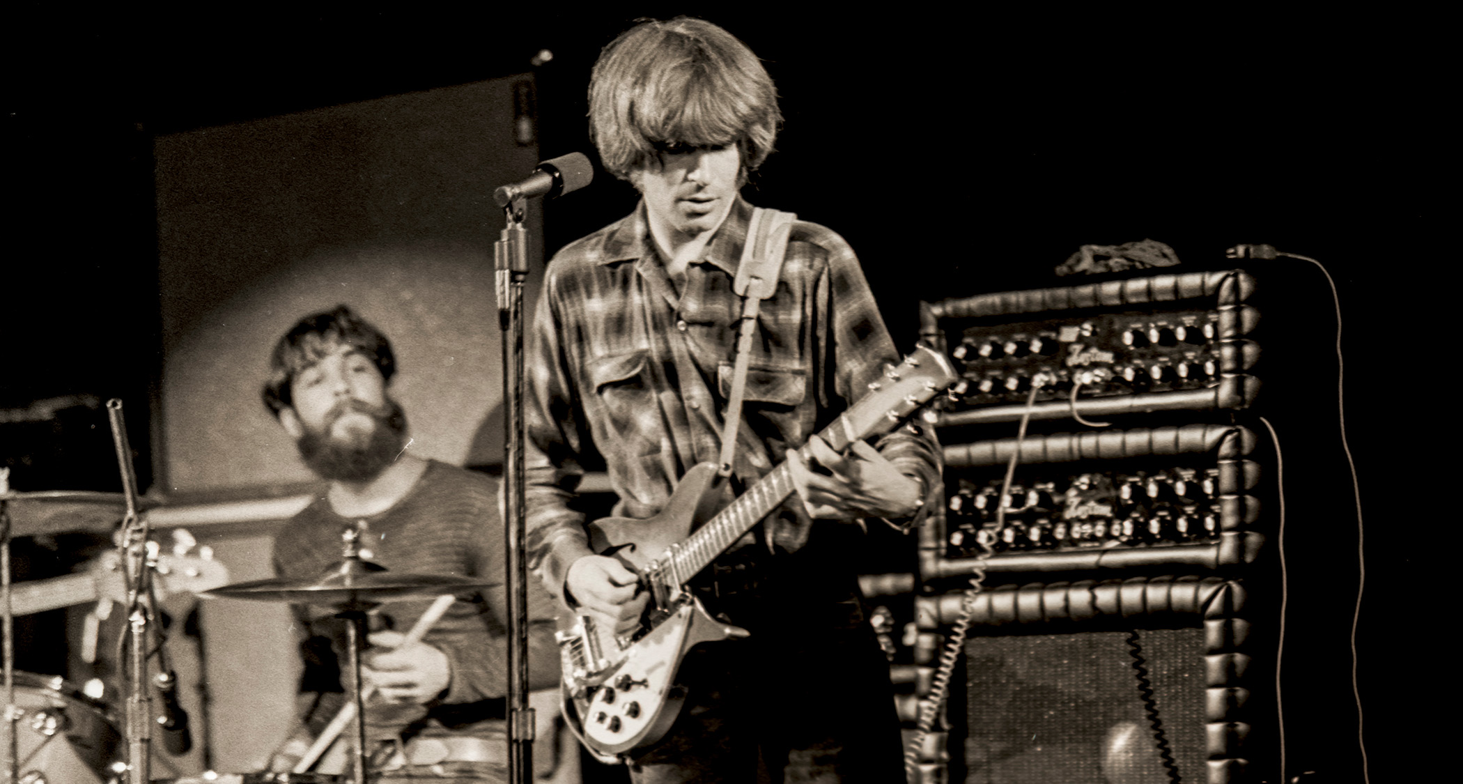 John Fogerty plays his Acme Rickenbacker onstage with Creedence Clearwater Revival in 1970, is Kustom &quot;tuck and roll&quot; amplifier stacks are visible in the background, as is a bearded Doug Clifford on drums.