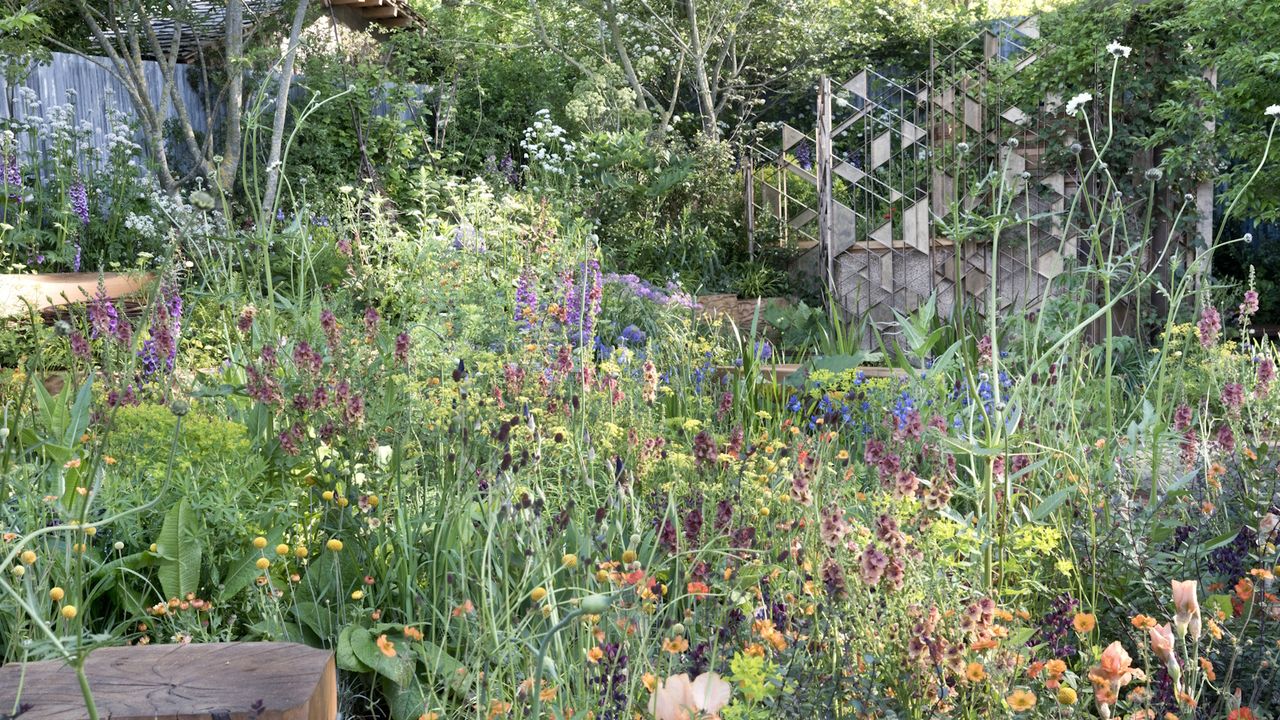 A garden planted with an abundance of flowers in muted pink, purple and apricot tones